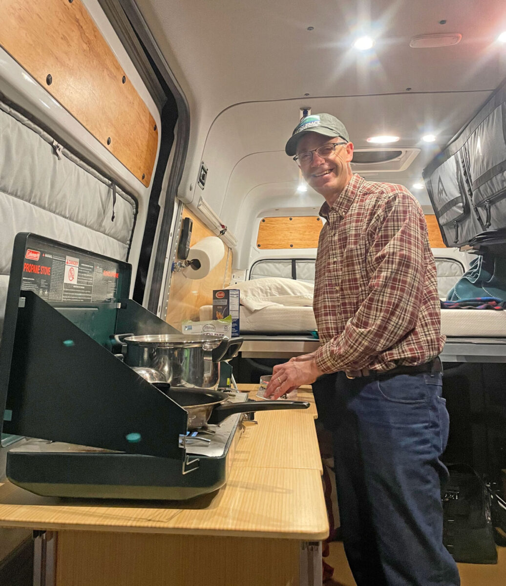 Hugh cooking using a camp stove inside a converted Sprinter cargo van