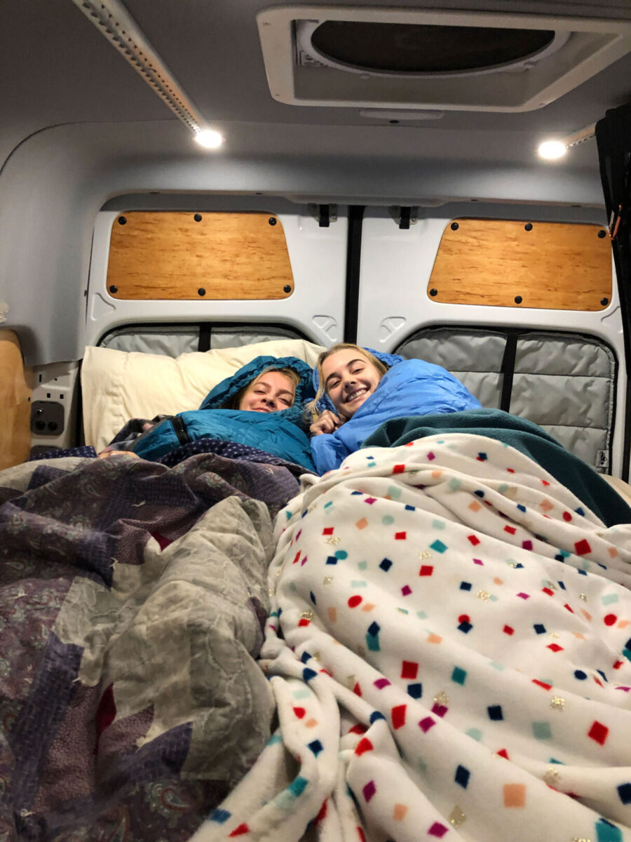 Two young women in sleeping bags in a converted Sprinter cargo van