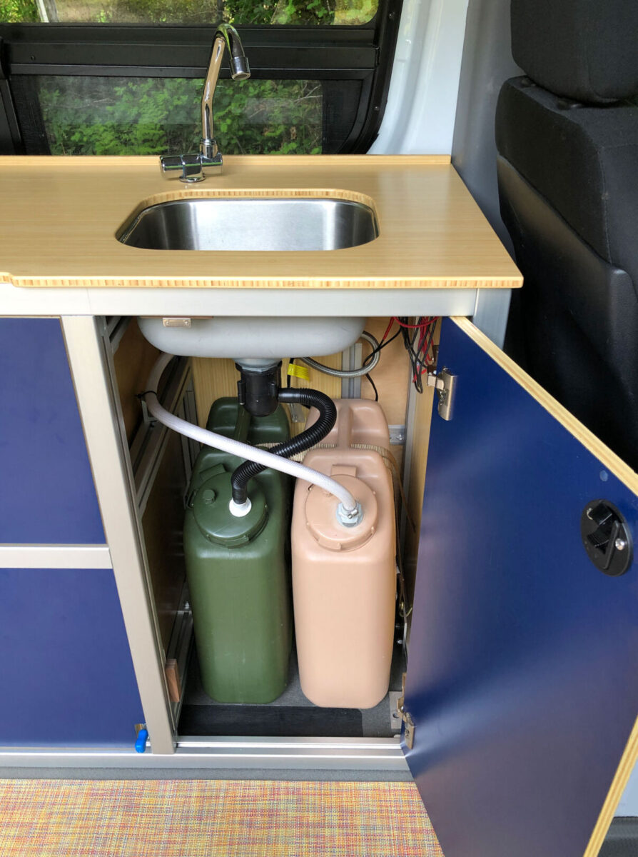 Van galley sink with door open showing water tanks
